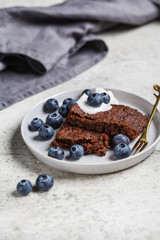 Vegan brownie - chocolate cake with coconut yogurt and blueberries on gray plate.