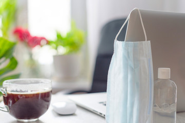 workplace at home by the window with a laptop, protective face mask and sanitizer, concept of quarantine during coronavirus pandemic in the world