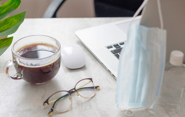 workplace at home with a laptop, protective face mask, glasses and monstera leaf, concept of quarantine during coronavirus pandemic in the world