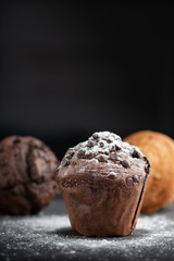 Chocolate muffin, cupcakes sprinkled with powdered sugar on a beautiful stone base. Sweet and delicious homemade bakery. Dark background
