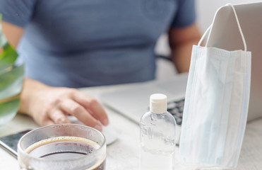 a man works at home with a laptop, a protective face mask, coffee and a sanitizer, quarantine due to the coronavirus pandemic