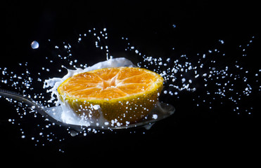 Fresh colorful orange fell into the milk until they splashed against the black background.