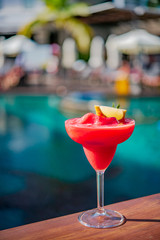 Close up a glass of red watermelon shake with slice lime cocktail with background of blurry swimming pool. Cocktail by the pool concept.