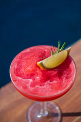 Close up a glass of red watermelon shake with slice lime cocktail with background of blue water pool. Copy space on top.