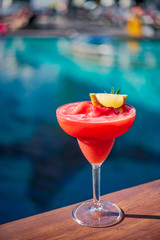 Close up a glass of red watermelon shake with slice lime cocktail with background of blurry swimming pool. Cocktail by the pool concept.