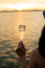 Young woman holding a glass of sparking wine looking at view of sunset from yacht.