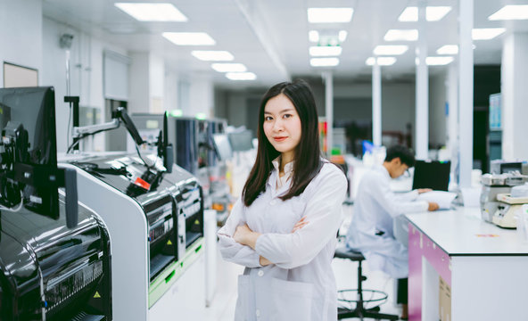 young smiling scientist in white lab coat standing with automation blood analyzer at medical laboratory