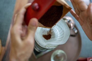 Close up of barista hand put grinded coffee in filter to make coffee dip.