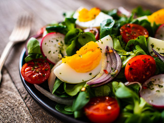 Salad with boiled egg and vegetables on wooden table
