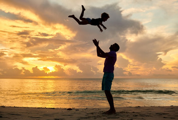 Father throws up son in the air on beach at sunset