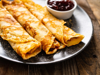 Sweet crepes with fruit jam on wooden table
