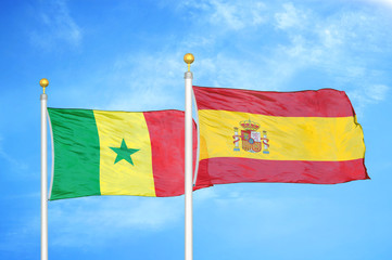 Senegal and Spain two flags on flagpoles and blue cloudy sky