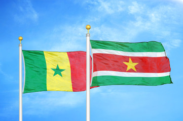 Senegal and Suriname two flags on flagpoles and blue cloudy sky