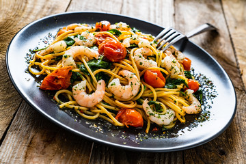 Spaghetti with prawns and vegetables on wooden background