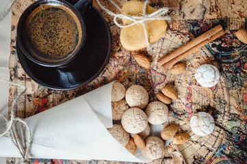 Almond biscuits amaretti with a cup of coffee. Almonds, gingerbread cookies and a cinnamon stick lie on an old map