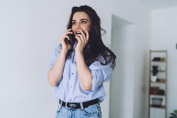 Pleasantly surprised woman talking on smartphone from home
