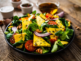 Fresh salad - blue cheese, cherry tomatoes, vegetables and walnuts on wooden background