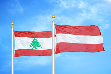 Lebanon and Austria  two flags on flagpoles and blue cloudy sky