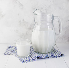 A jug of milk and a glass of milk on a light wooden table on a gray background. Concept of healthy natural products.