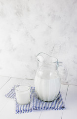 A jug of milk and a glass of milk on a light wooden table on a gray background. Concept of healthy natural products.