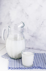 A jug of milk and a glass of milk on a light wooden table on a gray background. Concept of healthy...