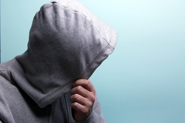Man covers his face with a hood, blue background
