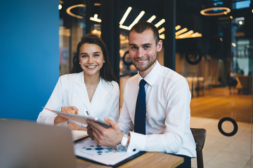 Portrait of cheerful corporate employees sitting at table with modern technology and smiling at...