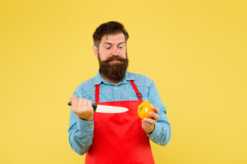 Chef prepares meal. cooking is his hobby. bearded man in cook uniform. confident housekeeper prepare tomato. mature man hold knife and vegetable. making fresh salad. professional chef in red apron