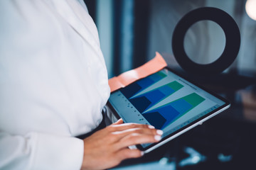 Female financial expert analyzing monetary gain from stock website connected to 4g on modern touch pad, cropped image of woman using gadget for checking data information from diagram infographics