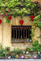 Fototapeta na wymiar Flowerpots with flowers, yellow wall and window with red chinese lanterns in Hoi An old town, Vietnam