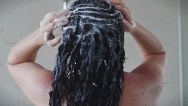 Pretty young girl washes away the shampoo from her hair while standing under a warm shower stream. Concept of cleanliness of hair and body, hygiene.