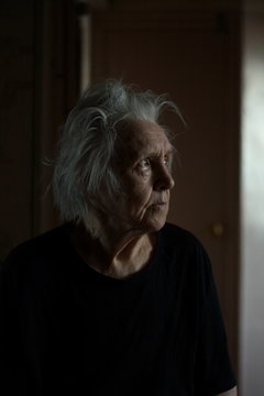 Portrait of grandmother at the home. Grandma sits in the dark and looks at the light.