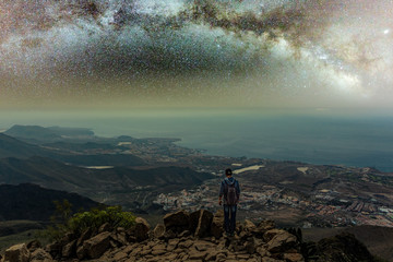 Obraz premium Traveler stays on top of mountain and enjoys the milky way view after sunset. Young tourist stand on the hill with colorful night sky on background. High ISO long exposure shot hight sky concept