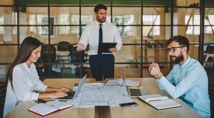 Group of young male and female colleagues cooperating on project ideas during work day in modern office interior with high speed internet connection for browsing information via laptop computers