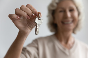 Head shot close up focus on keys from new apartment accommodation in hands of happy senior older woman. Excited smiling sincere middle aged mature grandmother celebrating purchase of house flat.