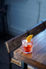 Negroni with a slice of orange on wooden table in a bar, cold colours, cold light, modern bar