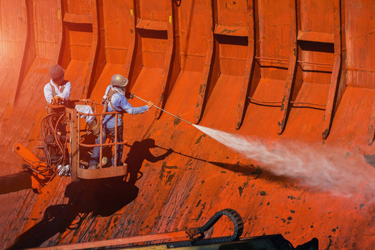 Washing and cleaning, worker High pressure water jet to cleaning with Old ship washing wearing safety harness with in side cargo hold under ship repair in floating dry dock in shipyard
