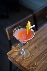 Cosmopolitan cocktail on wooden table in a cold light in a bar, top view