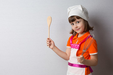 Fototapeta premium Girl cook holds a wooden spoon and a whisk in his hands. There is room for text on the left