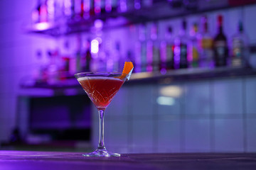 Cosmopolitan cocktail on wooden table in a pink neon light of a loft bar