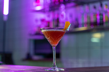 Cosmopolitan cocktail on wooden table in a pink neon light of a loft bar