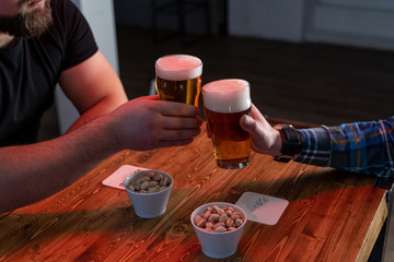 Men are clinking glasses with light beer over a table with beer snacks, in a pub with neon lights