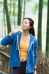 A young Asian woman resting and drinking water in a bamboo forest