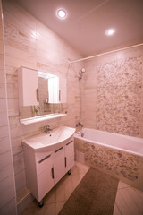 Bathroom in light beige brown and white tones. with a sink, a toilet bowl, a bathtub