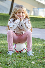 girl sitting on a soccer ball in the park