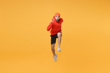 Fototapeta na wymiar Young bearded fitness sporty guy 20s sportsman in hat, hoodie, shorts spend weekend in home gym isolated on yellow wall background. Workout sport motivation lifestyle concept. Jumping like running.