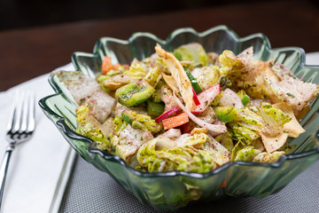 A view of a bowl of fattoush salad, in a restaurant or kitchen setting.