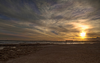 sunset on the sea, there is a bench on the shore