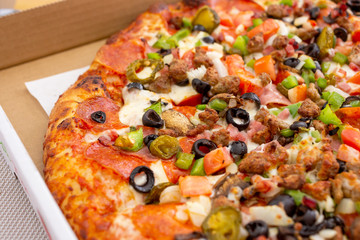 A closeup view of a supreme style pizza pie in a delivery box.