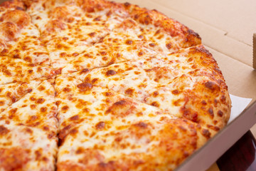 A view of a standard cheese pizza inside a pizza box, in a restaurant or kitchen setting.